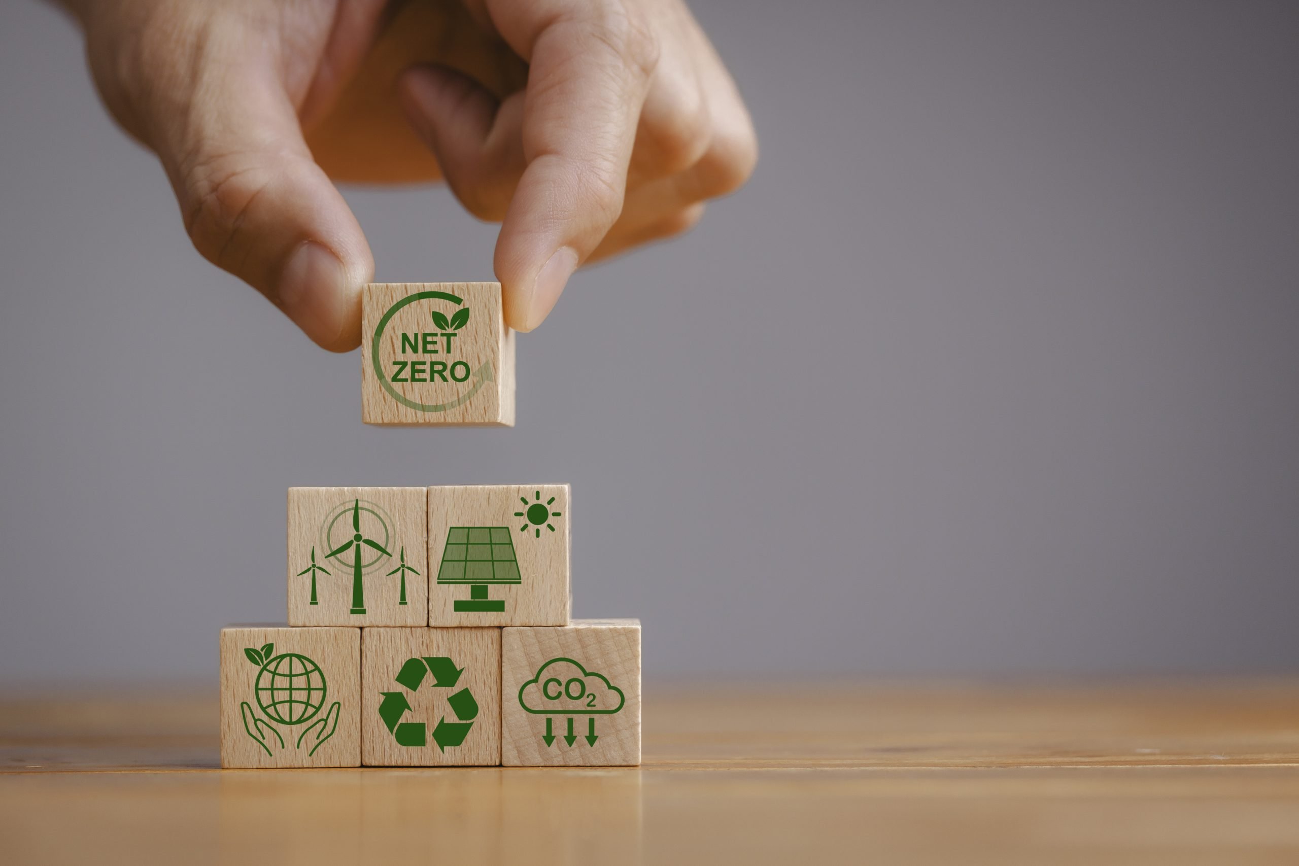 Net zero and carbon neutral concept. Net zero greenhouse gas emissions target. Climate neutral long term strategy. Hand put wooden cubes with green net zero icon and green icon on grey background.